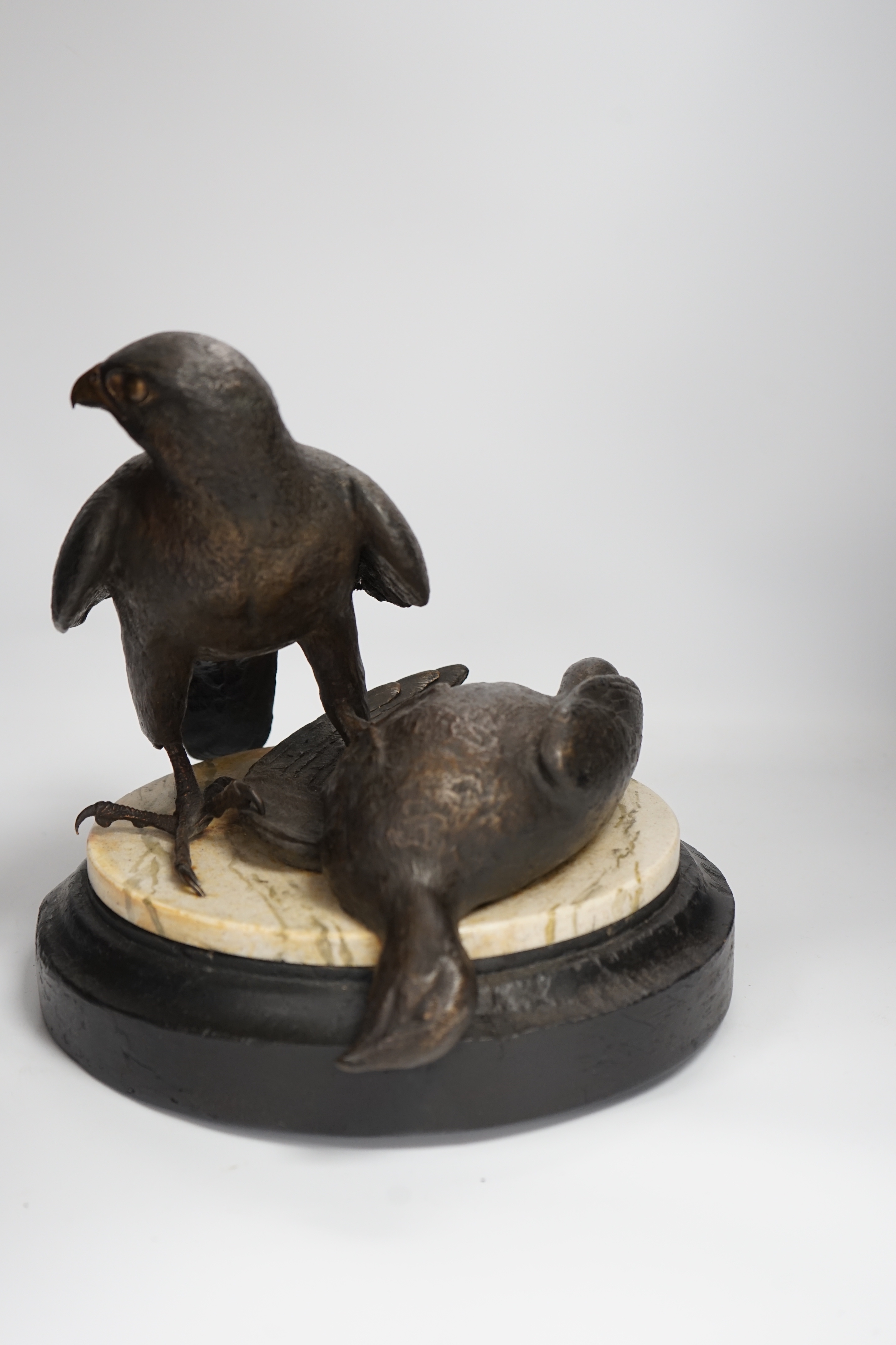 A limited edition bronze bird of prey with a kill, on a faux marble disc and painted wooden stand, 29cm high